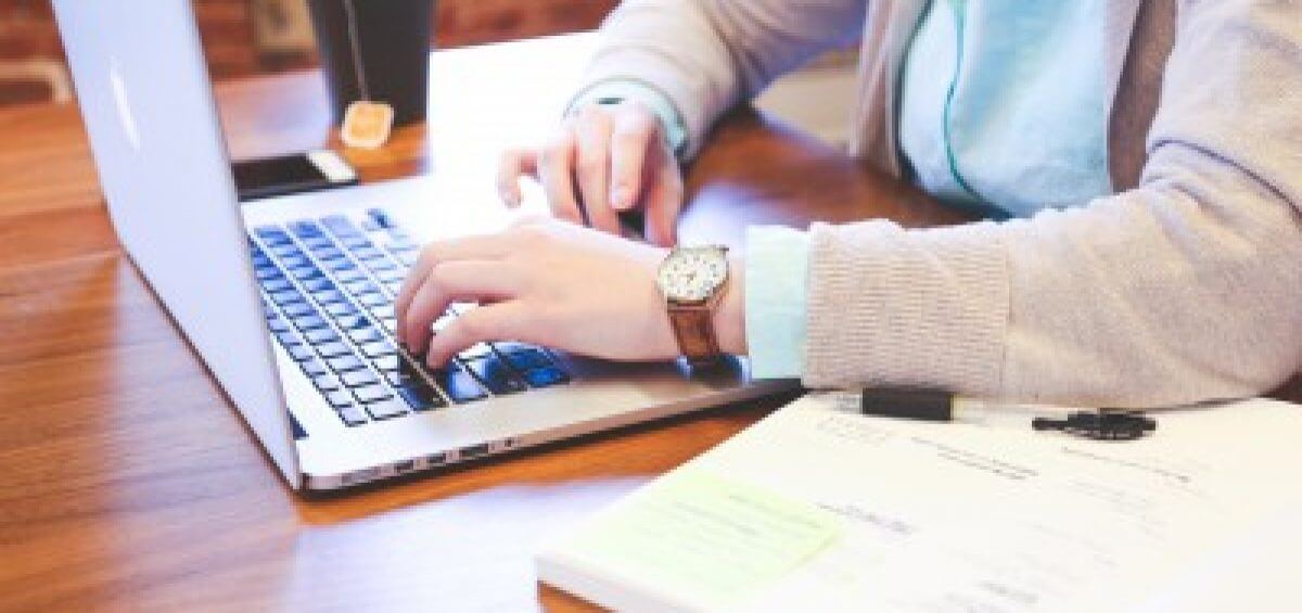 Young woman at Mac laptop with textbook open