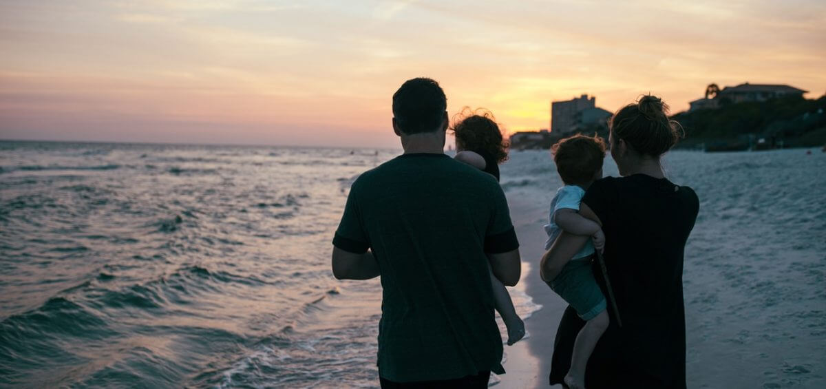 Young family walking on the shore of the beach with beautiful sunset