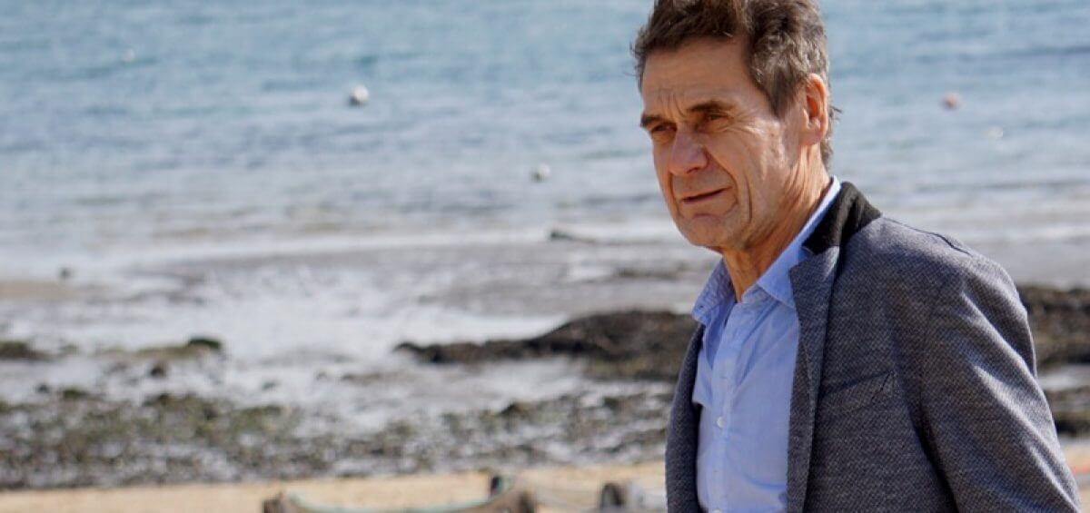 An older man looking pensive as he stands on the beach's shore