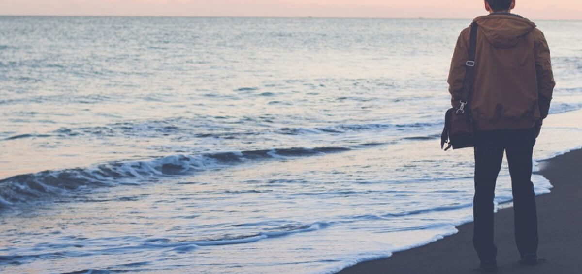 Young man standing on the shore of a beach staring into sunset