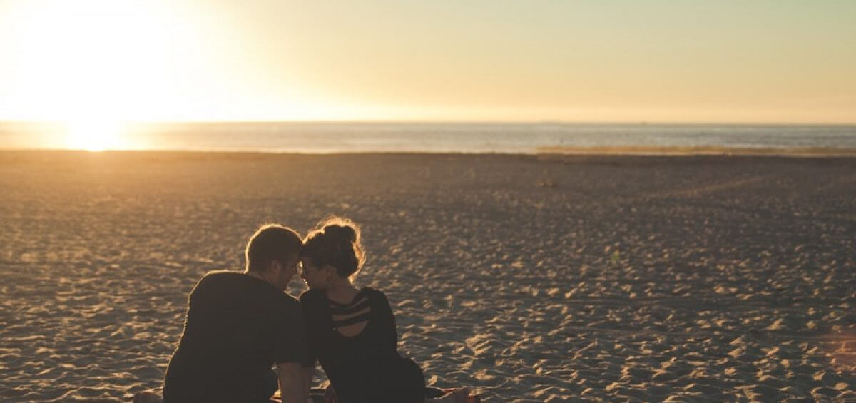In love couple sitting on beach as the sunsets