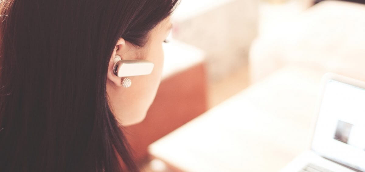Woman wearing earpiece while working on white laptop as she reads about the 457 Visa changes