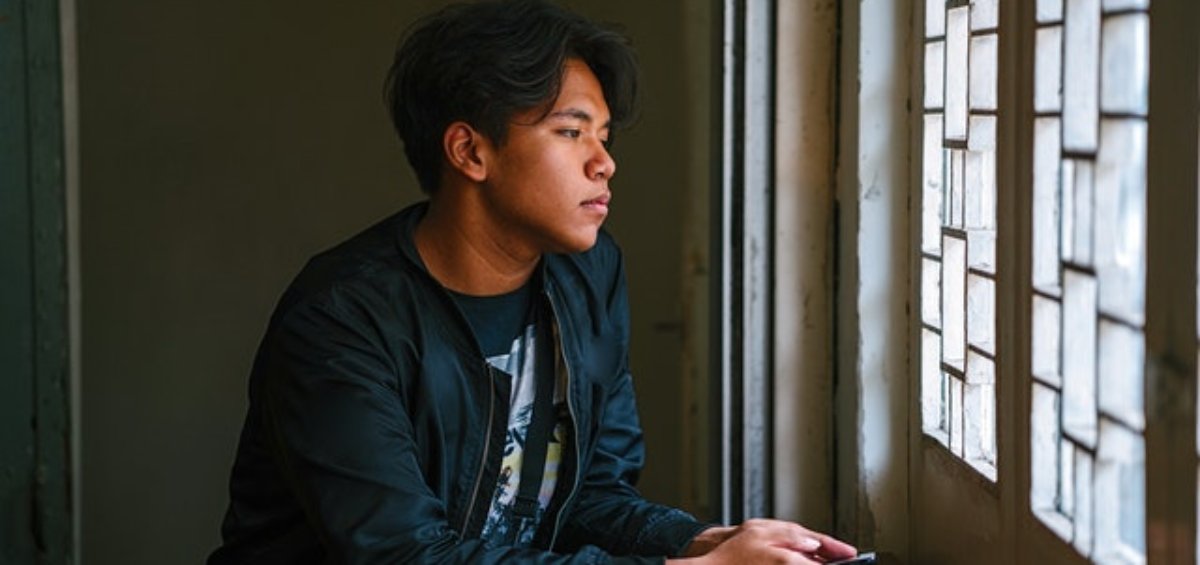 Young man looking outside the window thinking about his subclass 408 visa options