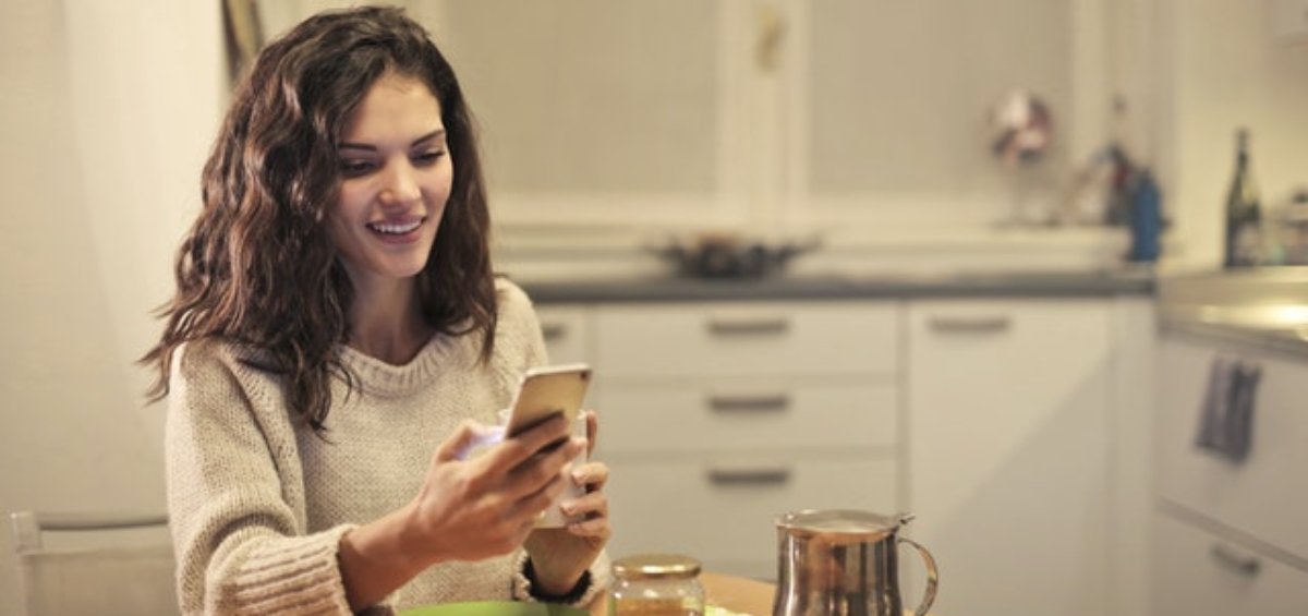 Young woman drinking tea and using smartphone as she explores support for visa holders